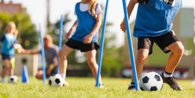 Slalom antrenmanında top sürüyor. Okul çocukları için futbol kampı. Çim sahada futbol antrenmanı ekipmanları