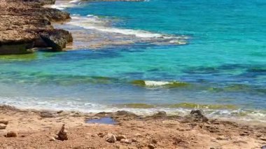 Resimli plaj, kumlu kıyıya vuran dalgalar. Deniz dalgaları kayalara çarpıyor. Kıbrıs Adası, Akdeniz.