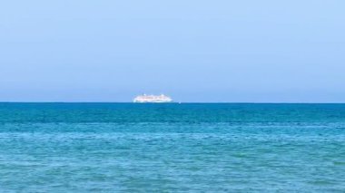 Resimli plaj, kumlu kıyıya vuran dalgalar. Deniz dalgaları kayalara çarpıyor. Kıbrıs adası, şemsiyeler, turist botları, Akdeniz.