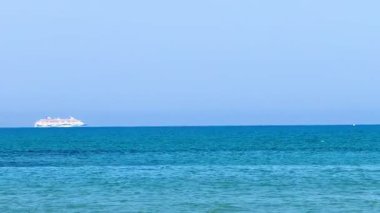 Resimli plaj, kumlu kıyıya vuran dalgalar. Deniz dalgaları kayalara çarpıyor. Kıbrıs adası, şemsiyeler, turist botları, Akdeniz.