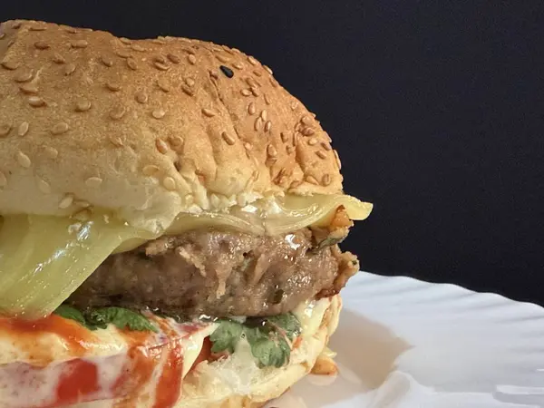 Beyaz tabakta domatesli ve yeşillikli büyük bir çizburger. Lezzetli, besleyici ve hazır yemek..