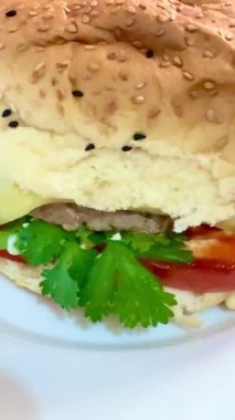 Beyaz tabakta domatesli ve yeşillikli büyük bir çizburger. Lezzetli, besleyici ve hazır yemek..