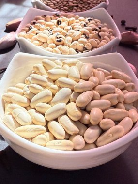 Beyaz fasulye, mercimek ve siyah bir yüzey üzerinde beyaz kâselerde siyah bezelyeler. Sağlıklı, sağlıklı, bitkisel gıdalar..