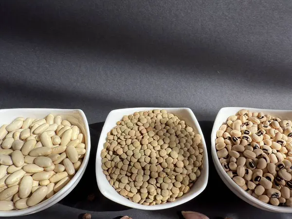 Beyaz fasulye, mercimek ve siyah bir yüzey üzerinde beyaz kâselerde siyah bezelyeler. Sağlıklı, sağlıklı, bitkisel gıdalar..