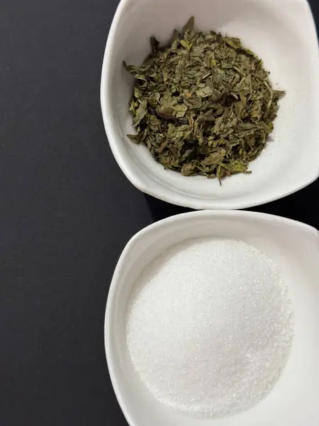 Koyu arkaplanda bir kase nane çayı ve şeker.