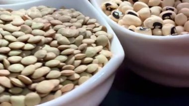 Beyaz fasulye, mercimek ve siyah bir yüzey üzerinde beyaz kâselerde siyah bezelyeler. Sağlıklı, sağlıklı, bitkisel gıdalar..