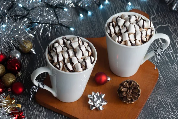 Hot Chocolate or Cocoa with Marshmallows Covered in Chocolate Sauce in Two Mugs with Festive Christmas Decorations