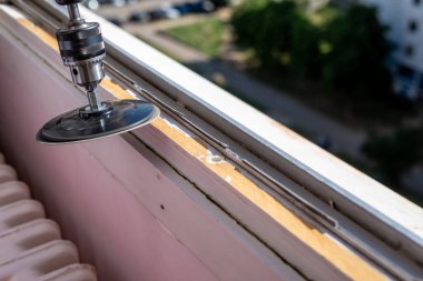 Sanding an old window frame during renovation work with a park of a residential city quarter in a background
