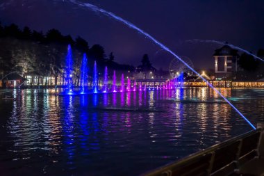 Sırbistan 'da fıskiyeli ve arka planında ağaçlar olan Zlatibor göletinin resimli gece sahnesi