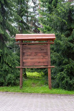 Arkasında çam ağaçları olan bilgi için sütunların üzerindeki rostat ahşap billboard.