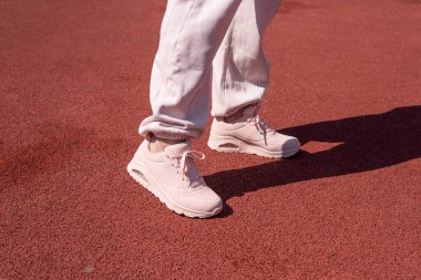 Spor ayakkabılı kadın bacakları ve pembe spor ayakkabıları parkta bir tartan patikasında duruyor.