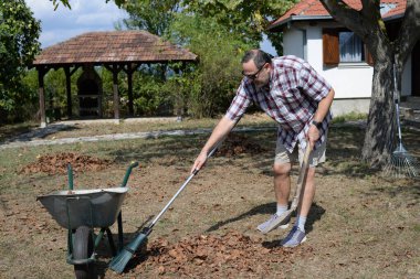 Adam bahçedeki kuru yaprakları temizliyor ve tırmıklıyor. Çöp toplama - Cumartesi temizlik günü