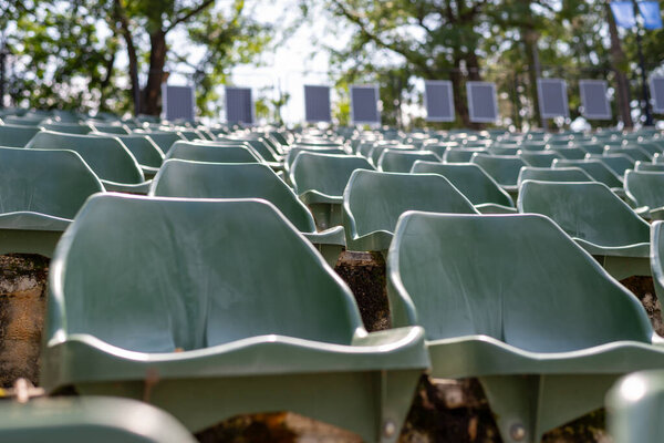 Крупный план нескольких зеленых пластиковых сидений, принадлежащих к большому каменному амфитеатру под открытым небом, с намеками на окружающую структуру на заднем плане
