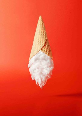 Canlı kırmızı arka planda havada duran dondurma külahı ve Noel Baba sakallı gerçeküstü bir kompozisyon. Asgari Noel tatlısı konsepti.