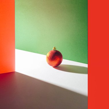 Geometrik renkli arka planda parlak kırmızı parıltılı tatil süsüsüyle serin sanatsal kompozisyon. Asgari Noel kavramı.