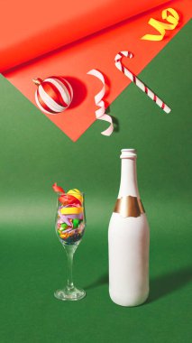 Renkli flamalarla dolu kristal bardaklı gerçek üstü sahne, Noel süsleri ve çift tonda şampanya şişesi yeşil ve kırmızı arka planda. Vintage Xmas parti konsepti.