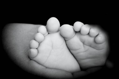 Baby feet held by mothers hand. Black background