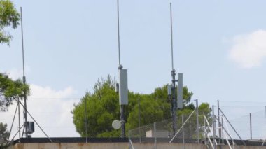 Düşük katlı bir yapının üzerine yerleştirilmiş 5G antenleri sizi geleceğe taşıyacak. Bu parlak ve çağdaş antenler güçlü bir çite ve uzun bir ağaca karşı bağlanmanın geleceğini temsil ediyor.. 