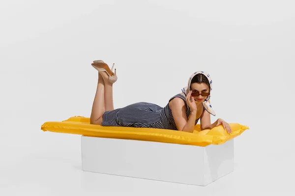 stock image Portrait of young beautiful woman in stylish clothes lying on inflatable mattress isolated on white background. Cruise. Concept of holidays, occupation, retro fashion, vintage style. Copy space for ad
