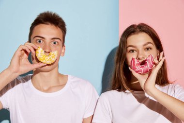 Genç insanların portresi. Mavi-pembe arka planda izole edilmiş donutlarla poz veren kadın ve erkek. Gençlik kültürü, moda, ilişki, duygu kavramı. İlan için alanı kopyala