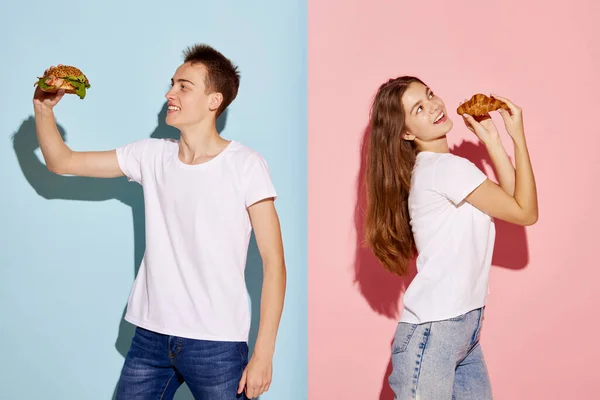 年轻人的画像 拿着汉堡包的男人和拿着羊角面包的女人在蓝色粉红的背景下摆出孤立的姿势 关于青年文化 情感的概念 广告的复制空间 — 图库照片