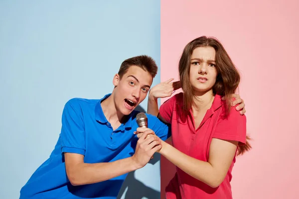 青いピンクの背景の上にマイクでポーズをとる若者 男と女の肖像画 マイクのための戦い 若者文化 ファッション 感情の概念 広告のコピースペース — ストック写真