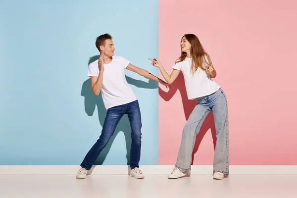 stock image Portrait of young couple, man and woman in casual clothes dancing isolated over blue-pink background. Friendship. Concept of youth culture, fashion, relationship, emotions. Copy space for ad