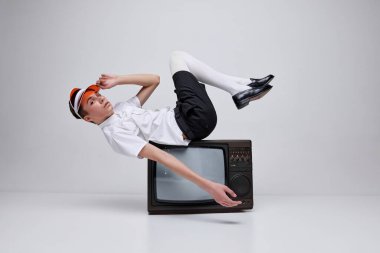 Tarz sahibi genç bir adamın portresi, gri arka planda izole edilmiş retro TV 'de poz veren bir çocuk. Moda gösterisi yayını. Modern moda kavramı, sanat fotoğrafçılığı, stil, nonoşluk, eşsizlik, reklam