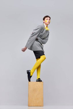 Gri arka planda izole edilmiş ceketli, ceketli ve sarı taytlı şık çocuk portresi. Tuhaf bir gençlik tarzı. Modern moda kavramı, sanat fotoğrafçılığı, stil, nonoşluk, eşsizlik, reklam