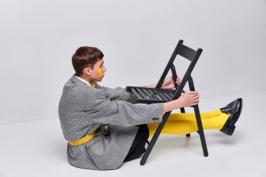 Gri arka planda izole edilmiş ceketli, ceketli ve sarı taytlı şık bir gencin portresi. Tuhaflık. Modern moda kavramı, sanat fotoğrafçılığı, stil, nonoşluk, eşsizlik, reklam