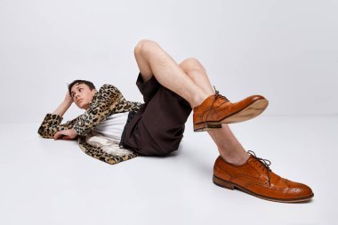 Hayvan desenli ceketli şık bir gencin portresi ve gri arka planda zemin üzerinde duran klasik spor ayakkabılı. Modern moda kavramı, sanat fotoğrafçılığı, stil, nonoşluk, eşsizlik, reklam