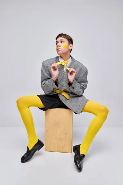 灰色の背景に隔離されたジャケット ブレザー 黄色のタイツに身を包んだスタイリッシュな少年の肖像画 スタイリッシュな十代の生活 現代ファッション アート写真 スタイル クィア ユニークさ 広告のコンセプト — ストック写真