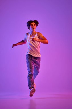 Beyaz tişörtlü genç kaslı adamın portresi, neon ışıkta mor arka planda poz veren atlet. Gençlik kavramı, gündelik moda, yüz ifadesi, duygular, yaşam tarzı, reklam