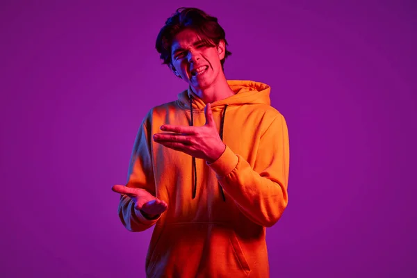 ネオンの光の中で紫の背景に隔離されたポーズカジュアルなパーカーの若い男の肖像画 積極的に議論 若者の概念 カジュアルファッション 顔の表情 ライフスタイル — ストック写真