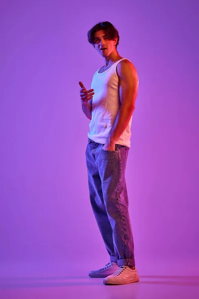 白いTシャツを着た若い筋肉の男の肖像 ネオンの光の中で紫色の背景の上にポーズをシングル 薄汚い顔だ 若者の概念 カジュアルファッション 顔の表情 ライフスタイル — ストック写真