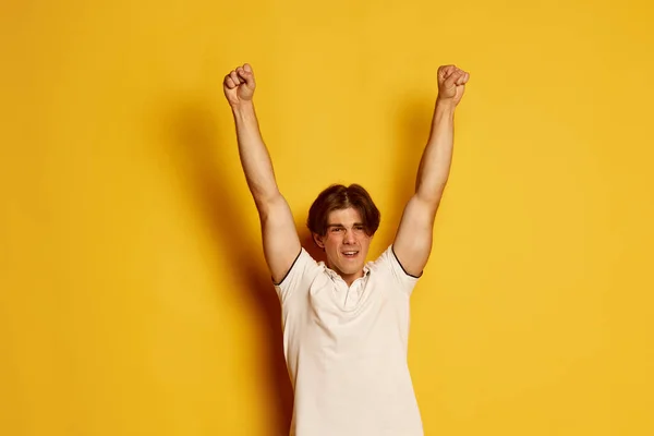 黄色の背景に勝利の表情でポーズをとったカジュアルな白いTシャツ姿の若い男の肖像 成功だ 若者の概念 カジュアルファッション 顔の表情 ライフスタイル — ストック写真