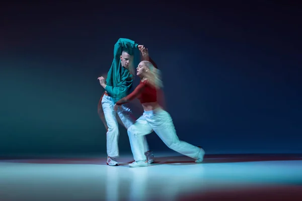 ステージ上でパフォーマンスする若いカップル 男性と女性の肖像は 混合光と濃い青の背景に隔離されています ヒップホップダンス 若者文化 アクティブライフスタイル ストリートダンス 広告の概念 — ストック写真