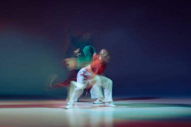 Koyu mavi arka planda karışık ışıklarla dans eden genç adam ve kadının portresi. Sportif yaşam tarzı. Hareket kavramı, gençlik kültürü, aktif yaşam tarzı, aksiyon, sokak dansı, reklam