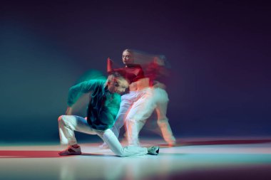 Hip-hop dansı yapan genç sporcu erkek ve kadın portresi koyu mavi arka planda karışık ışıklarla izole edilmiş. Hareket kavramı, gençlik kültürü, aktif yaşam tarzı, aksiyon, sokak dansı, reklam