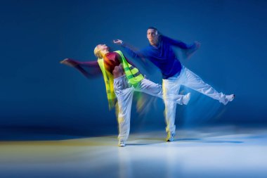 Koyu mavi arka planda karışık ışıklarla dans eden genç adam ve kadının portresi. Senkronize. Hareket kavramı, gençlik kültürü, aktif yaşam tarzı, aksiyon, sokak dansı, reklam