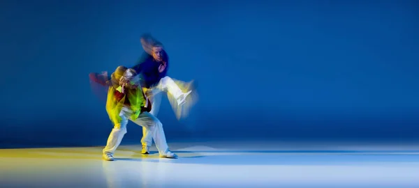 Portrait of young man and woman dancing, performing hip-hop isolated on blue yellow background with mixed lights. Flyer. Concept of movement, youth culture, active lifestyle, action, street dance, ad