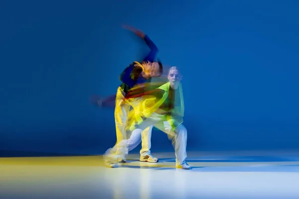 Portrait of young man and woman dancing isolated over blue yellow background with mixed lights. Expression of freedom. Concept of movement, youth culture, active lifestyle, action, street dance, ad