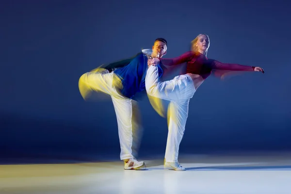 stock image Portrait of young man and woman dancing isolated over dark blue background with mixed lights. Hip-hop synchronization. Concept of movement, youth culture, active lifestyle, action, street dance, ad