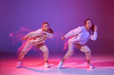 Hip-hop dansı yapan iki genç kızın portresi karışık ışıkla karışık menekşe arka planında izole edilmiş. Hareket kavramı, gençlik kültürü, aktif yaşam tarzı, aksiyon, sokak dansı