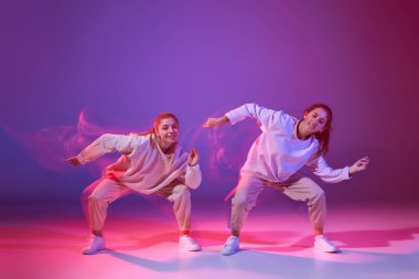 Hip-hop dansı yapan iki genç kızın portresi karışık ışıkla karışık mor arka planda izole edilmiş. Hareket kavramı, gençlik kültürü, aktif yaşam tarzı, aksiyon, sokak dansı