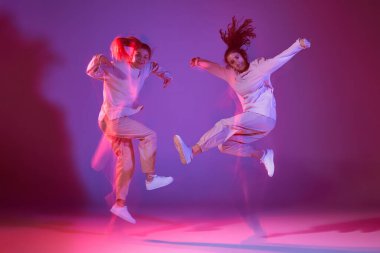 Hip-hop dansı yapan iki genç kızın portresi karışık ışıkla karışık menekşe arka planında izole edilmiş. Bir atlayışta. Hareket kavramı, gençlik kültürü, aktif yaşam tarzı, aksiyon, sokak dansı