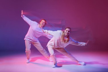 Hip-hop dansı yapan iki genç kız karışık ışıkla karışık mor arka planda izole edilmiş. Hareketlerin koordinasyonu. Hareket kavramı, gençlik kültürü, aktif yaşam tarzı, aksiyon, sokak dansı