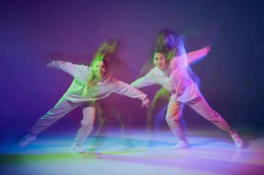 Hip-hop dansı yapan genç kızların portresi karışık ışıkla karışık mavi mor arka planda izole edilmiş. Arkadaşlık. Hareket kavramı, gençlik kültürü, aktif yaşam tarzı, aksiyon, sokak dansı