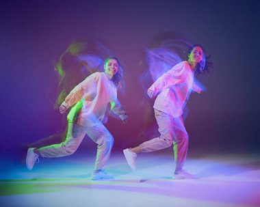 Hip-hop dansı yapan genç kızların portresi karışık ışıkla karışık mavi mor arka planda izole edilmiş. Mutlu görünüyorsun. Hareket kavramı, gençlik kültürü, aktif yaşam tarzı, aksiyon, sokak dansı