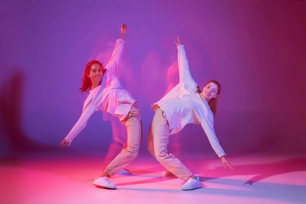 ネオンのグラデーションを背景に 光が入り混じったヒップホップを踊る2人の少女のポートレート 柔軟性 若者文化 アクティブライフスタイル アクション ストリートダンスの概念 — ストック写真